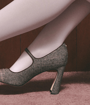 On-foot view of textured metallic Mary Jane pumps with a sculpted heel, styled with white tights.