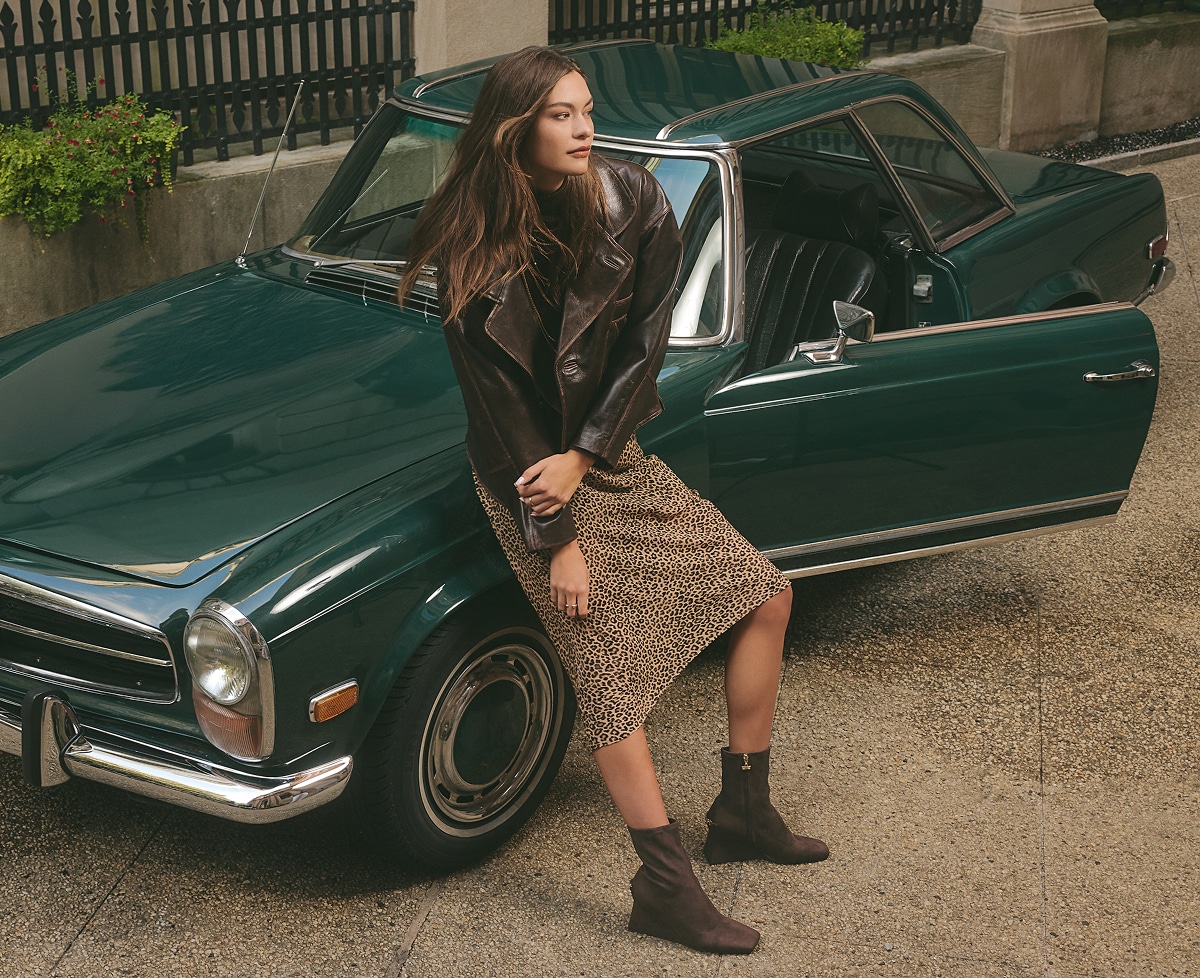woman leaning against a vintage car while wearing the lia wedge bootie in dark chocolate
