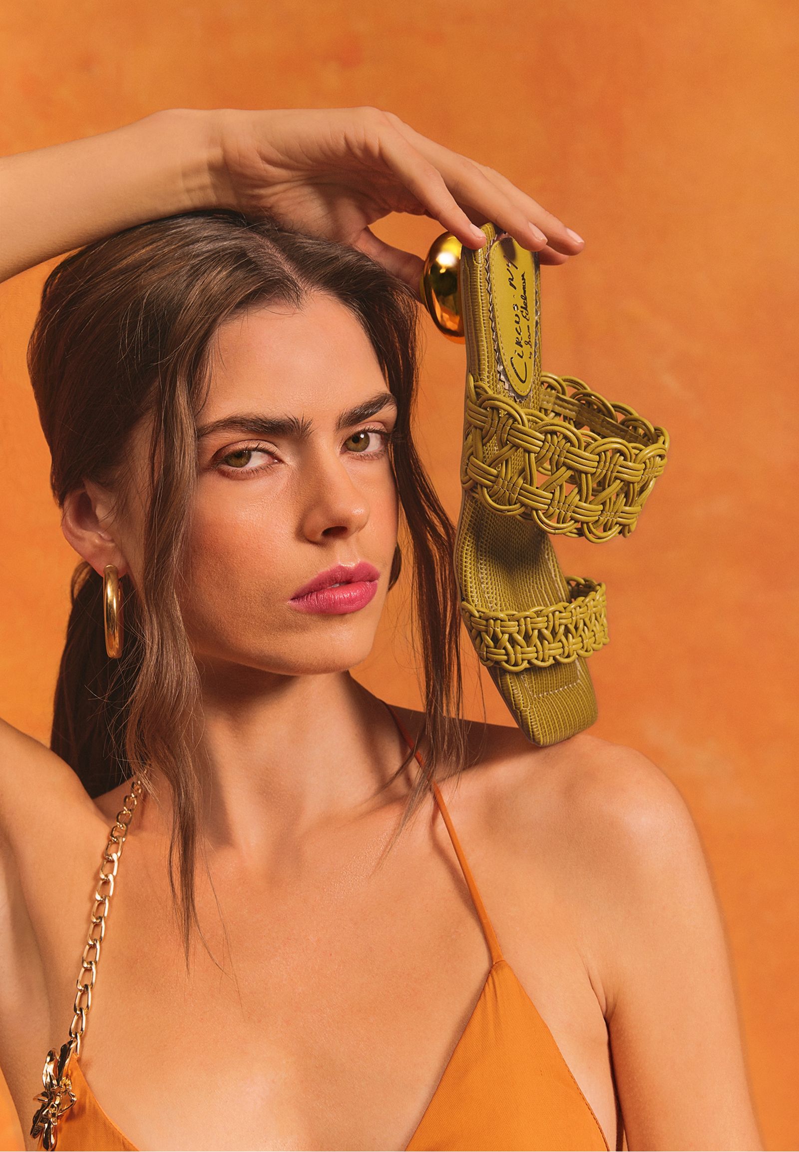 Model holding the Circus NY Clover slide sandal in lime leather with woven braided straps and gold round heel.