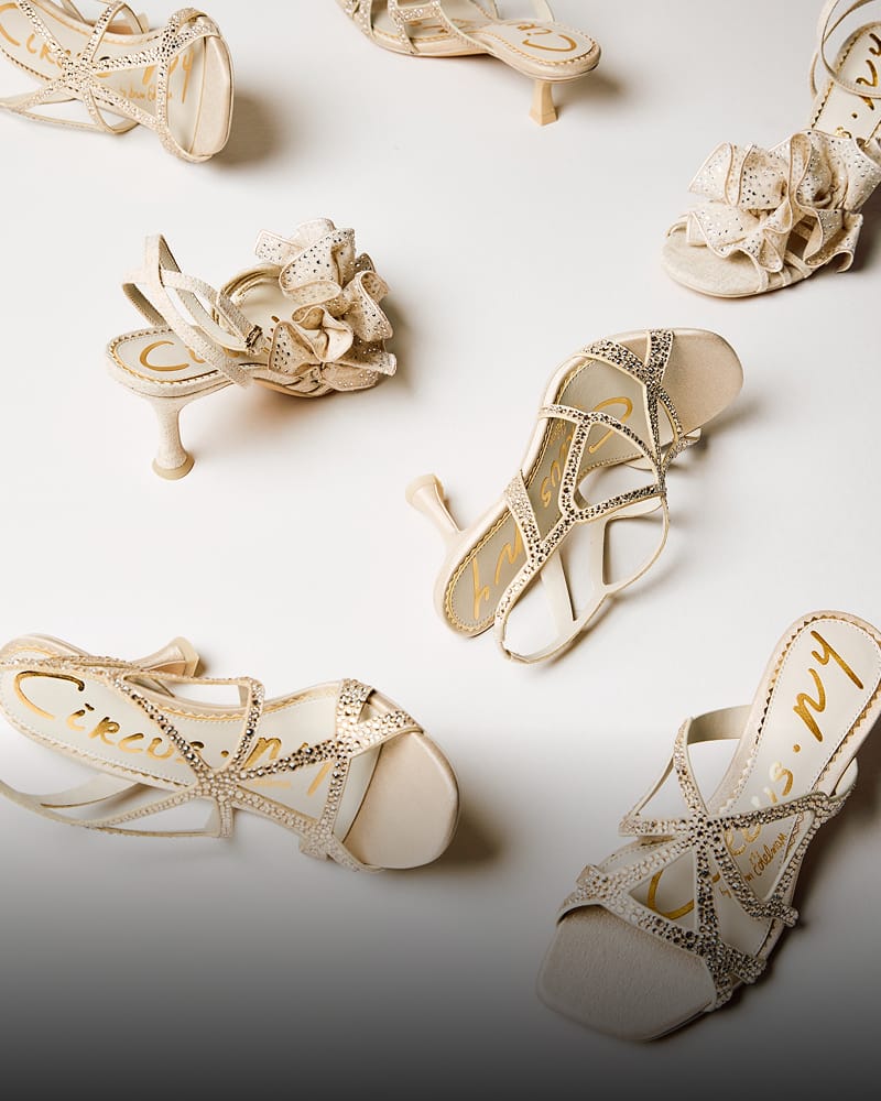 Circus NY heeled sandals in seashell white with rhinestone and ruffled strap details on a white background.